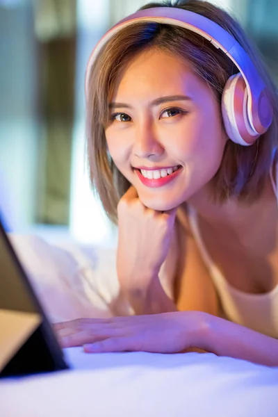 woman watch a video by digital tablet and wear headset on the bed at night