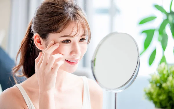 close up of beauty asian woman look her good skin near eyes in mirror at home