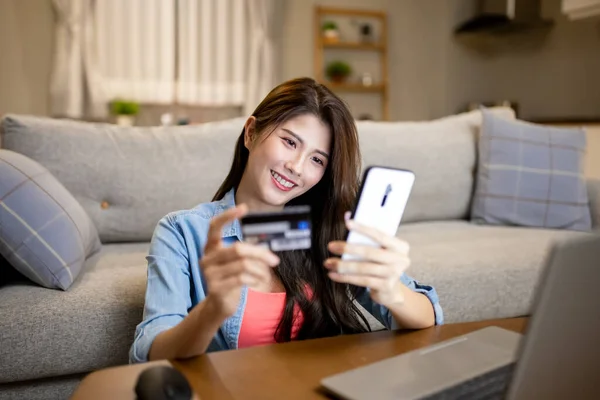 asian woman shopping on the internet and pay bill by credit card with smartphone at home