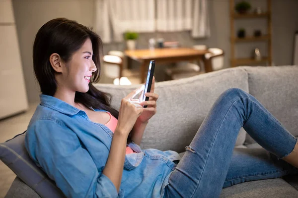 亚洲的年轻女子正在使用智能手机 悠闲地躺在家里客厅的沙发上 — 图库照片