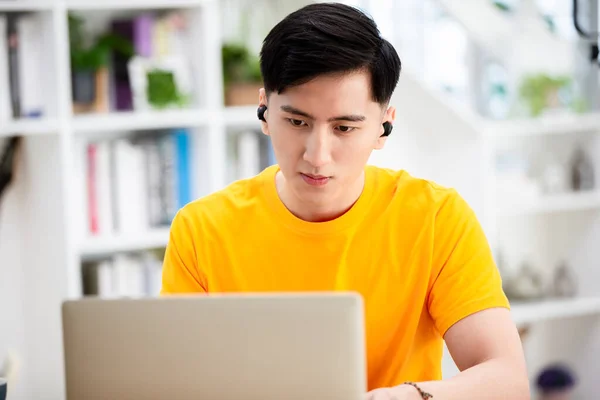 亚洲的年轻男生在家里用无线耳塞开设在线语言课程 并通过笔记本电脑搜索信息 — 图库照片