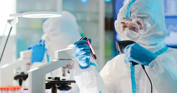 アジアの男性科学者の研究者は 隔離ガウンや保護服や外科的フェイスマスクでコロナウイルスの陽性血液検査結果をスキャンします — ストック写真