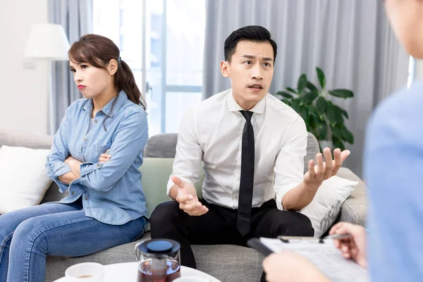 Young unhappy asian couple having marriage counseling and the husband is complaining
