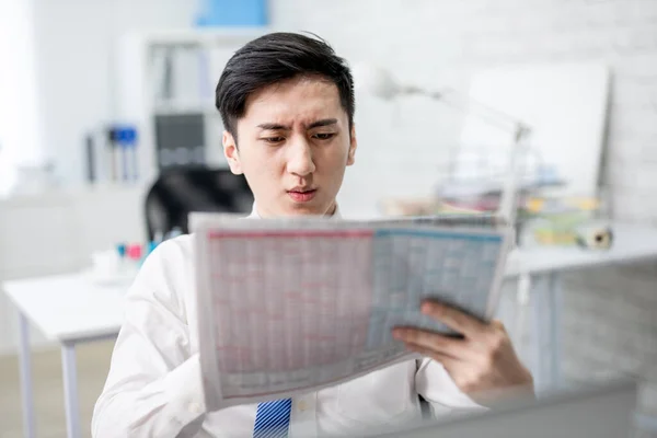 アジアの若いビジネスマンは新聞を読んでいて予期せぬ偽のニュースにショックを受け — ストック写真
