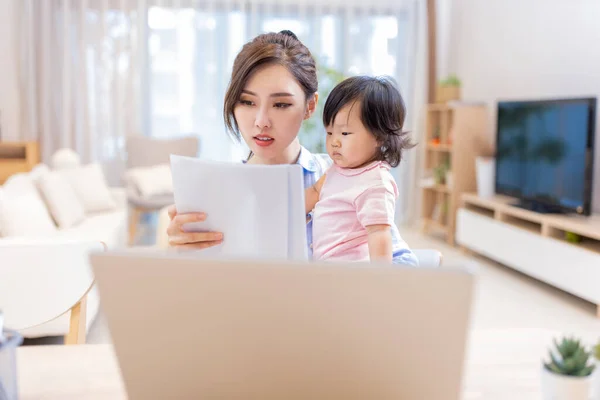 亚洲女商人在家里用笔记本电脑工作 照顾女儿 — 图库照片