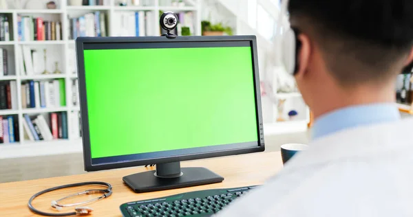 亚洲男性医生佩戴耳机的后视镜和带绿色屏风的电脑显示器 — 图库照片