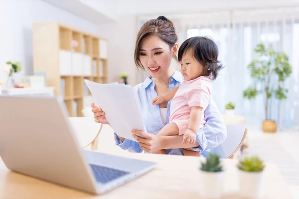asian business woman works from home by laptop and takes care of her daughter
