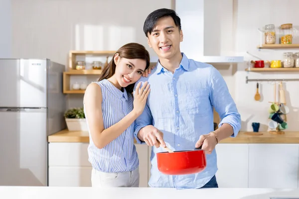 家庭のキッチンで料理をしながらアジア系の若いカップルが笑顔で — ストック写真