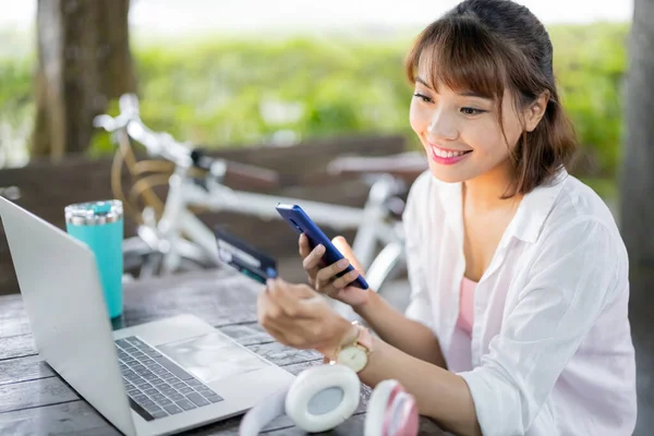 亚洲女青年在公园里用智能手机和笔记本电脑用信用卡付帐 — 图库照片