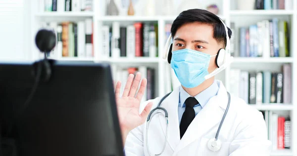 テレメディシンの概念 アジアの男性医師は インターネット上の症状について患者と話をし 顔のマスクとの議論を行う — ストック写真
