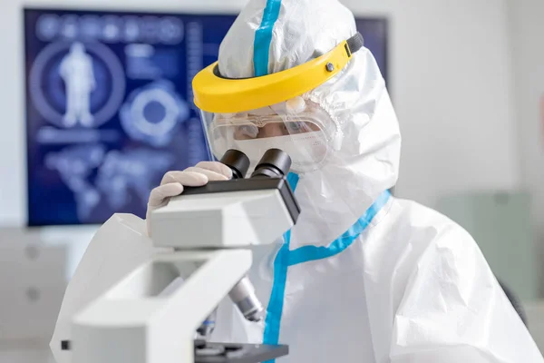 隔離ガウンや保護服や外科用フェイスマスクを身に着けているアジアの医師は 研究室で顕微鏡を見て — ストック写真