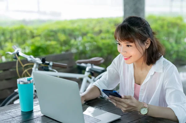 アジアの若い女性は公園で働くためにスマートフォンやラップトップを使用しています — ストック写真