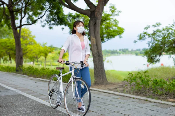 Asian female wearing protective mask for covid-19 epidemic virus with bicycle in the park
