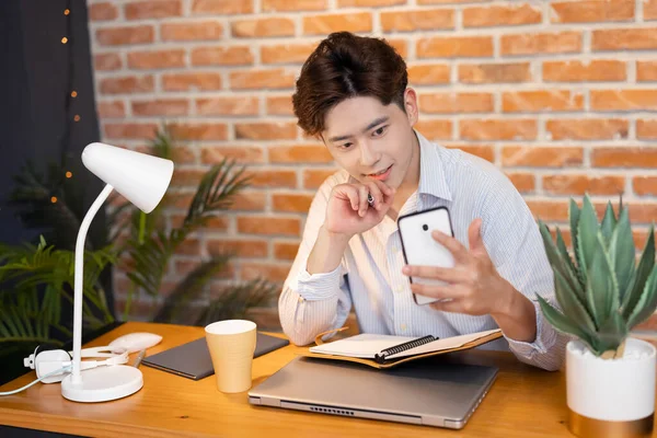 아시아인젊은 사업가는 스마트폰을 사용하여 비디오 회의에 참여하고 집에서 필기를 — 스톡 사진