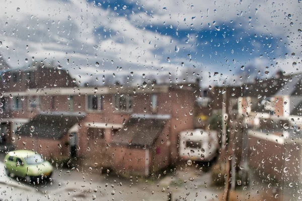 Common dutch suburb seen through a window wet by rain
