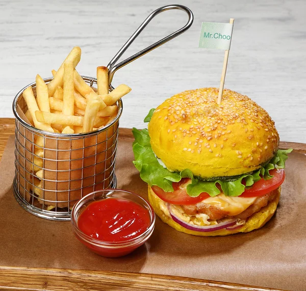 Burger with chicken, French fries, sauce, on a wooden board.