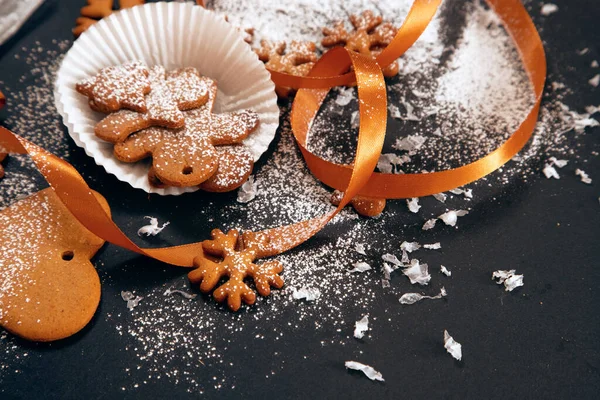 クリスマスの焼きたてのジンジャーブレッドクッキーは 黒を背景に雪の結晶とリボンで粉砂糖を振りかけた 休日の食べ物 自家製のベーキング クリスマスと新年の伝統 — ストック写真
