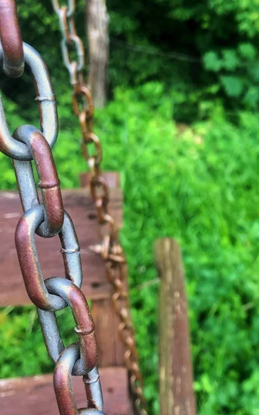 Onderdeel van een oude roestige bruine ijzeren ketting onder groene vegetatie — Stockfoto