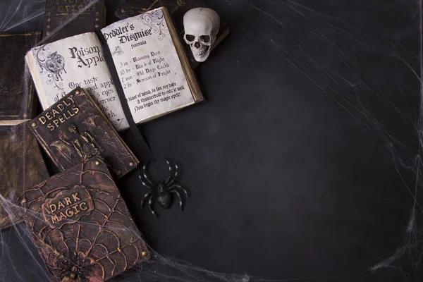 Old spell books with spider webs and a skull on a chalkboard background for Halloween.