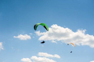 İki paraşütler bulutlar arka planı mavi gökyüzünde uçan. Güneşli bir havada yamaç paraşütü.