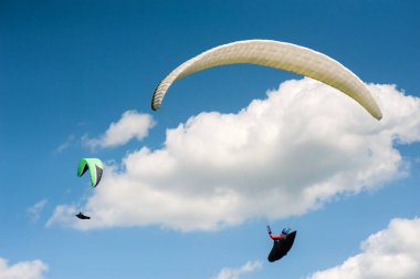 İki paraşütler bulutlar arka planı mavi gökyüzünde uçan. Güneşli bir havada yamaç paraşütü.
