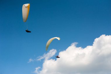 İki paraşütler bulutlar arka planı mavi gökyüzünde uçan. Güneşli bir havada yamaç paraşütü.