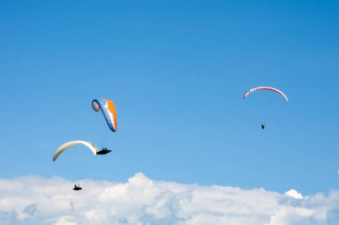 Üç paraşütler bulutlar arka planı mavi gökyüzünde uçan. Güneşli bir havada yamaç paraşütü.