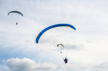 Üç paraşütler bulutlar arka planı mavi gökyüzünde uçan. Güneşli bir havada yamaç paraşütü.