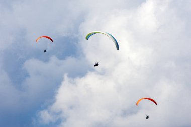 Üç paraşütler bulutlar arka planı mavi gökyüzünde uçan. Güneşli bir havada yamaç paraşütü.
