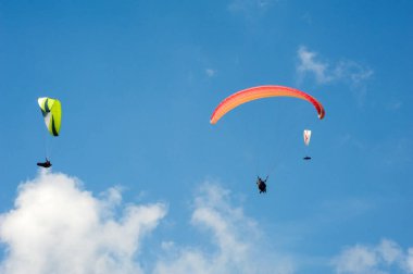Üç paraşütler bulutlar arka planı mavi gökyüzünde uçan. Güneşli bir havada yamaç paraşütü.