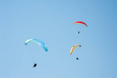 Üç paraşütler bulutlar arka planı mavi gökyüzünde uçan. Güneşli bir havada yamaç paraşütü.