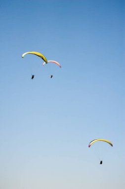 Üç paraşütler bulutlar arka planı mavi gökyüzünde uçan. Güneşli bir havada yamaç paraşütü.