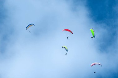 Bulutlar arka planı mavi gökyüzünde uçan paraşütler grubudur. Güneşli bir havada yamaç paraşütü.