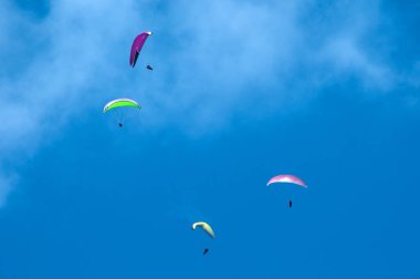 Bulutlar arka planı mavi gökyüzünde uçan paraşütler grubudur. Güneşli bir havada yamaç paraşütü.