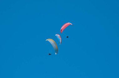 Bulutlar arka planı mavi gökyüzünde uçan paraşütler grubudur. Güneşli bir havada yamaç paraşütü.