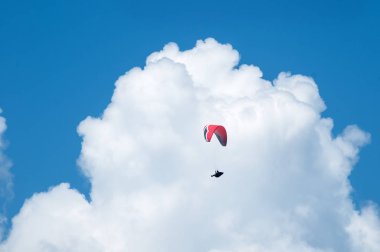 Bulutlar arka planı mavi gökyüzünde uçan bir yamaçparaşütü. Güneşli bir havada yamaç paraşütü.