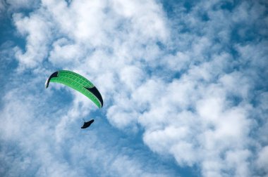 Bulutlar arka planı mavi gökyüzünde uçan bir yamaçparaşütü. Güneşli bir havada yamaç paraşütü.