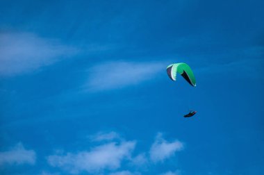 Bulutlar arka planı mavi gökyüzünde uçan bir yamaçparaşütü. Güneşli bir havada yamaç paraşütü.