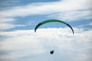 Bulutlar arka planı mavi gökyüzünde uçan bir yamaçparaşütü. Güneşli bir havada yamaç paraşütü.