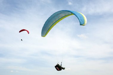 İki paraşütler bulutlar arka planı mavi gökyüzünde uçan. Güneşli bir havada yamaç paraşütü.
