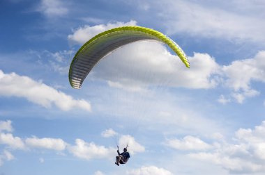 Sarı ve yeşil Yamaçparaşütü bulutlar arka planı mavi gökyüzünde uçuyor. 
