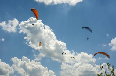 Büyük bir grup yamaç paraşütü mavi gökyüzünde bulutlara karşı uçuyor.. 