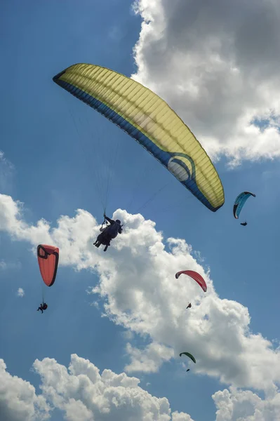 Büyük bir grup yamaç paraşütü mavi gökyüzünde bulutlara karşı uçuyor.. 