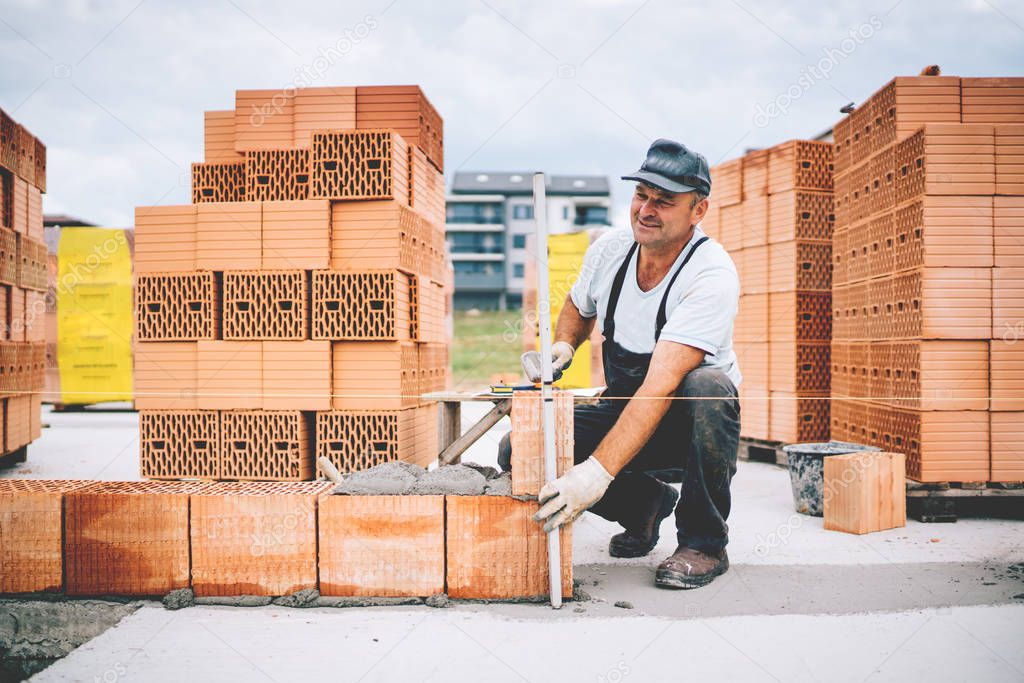 Industrial worker using leveler and tools for building exterior walls with bricks and mortar