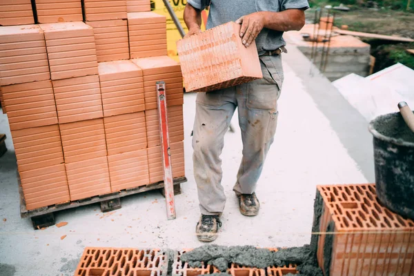 Industrial worker moving bricks and using tools for building exterior walls with bricks and mortar