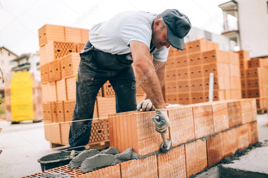 industrial worker building exterior walls, using hammer for laying bricks in cement. Detail of worker with tools and concrete
