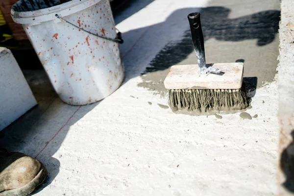 industrial tools on construction site, painters brush with waterproof sealant on concrete surface