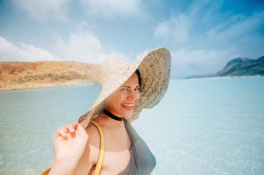 Gülümseyen kadın plajda, hasır şapka ve yüzme giysileri giyiyor. Güneşli bir günde Yunanistan dalgaları. Geniş açı çekim