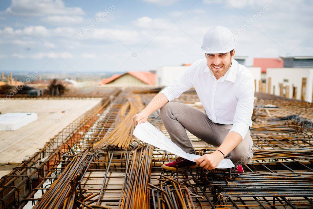 Smiling architect engineer on construction site, reading blueprints and coordinating workers