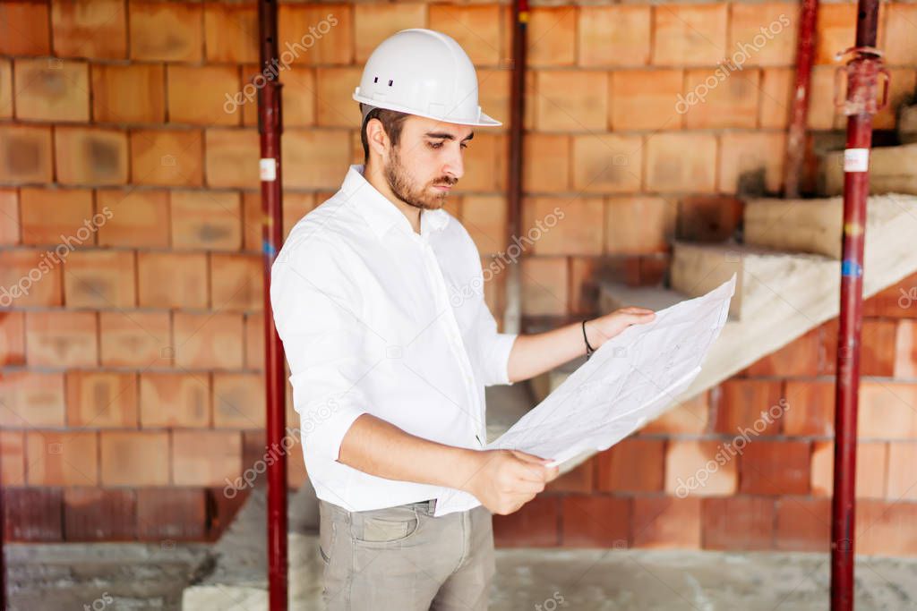 Construction engineer working on site, man reading paper plans and supervising works